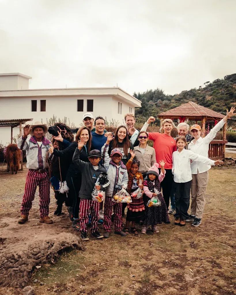 Group of people posing outdoors in front of a building, some smiling and waving.