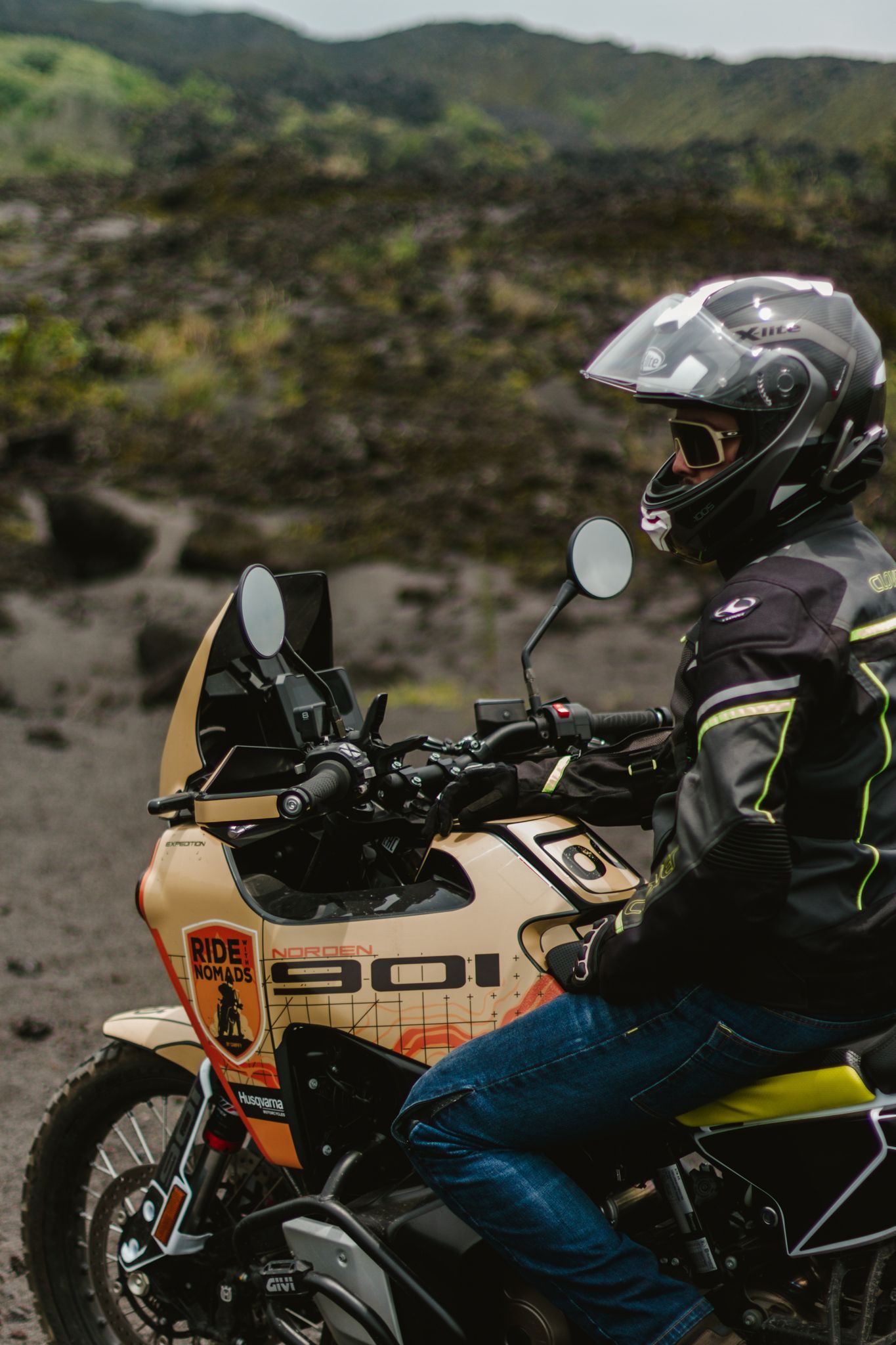Motorcyclist in black gear riding a white adventure bike on a rocky trail in a mountainous landscape