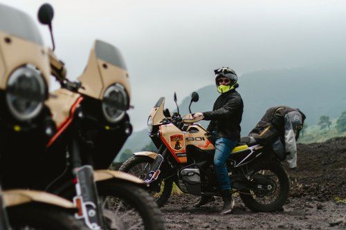Motorcyclists with adventure bikes on a muddy mountain road in misty weather