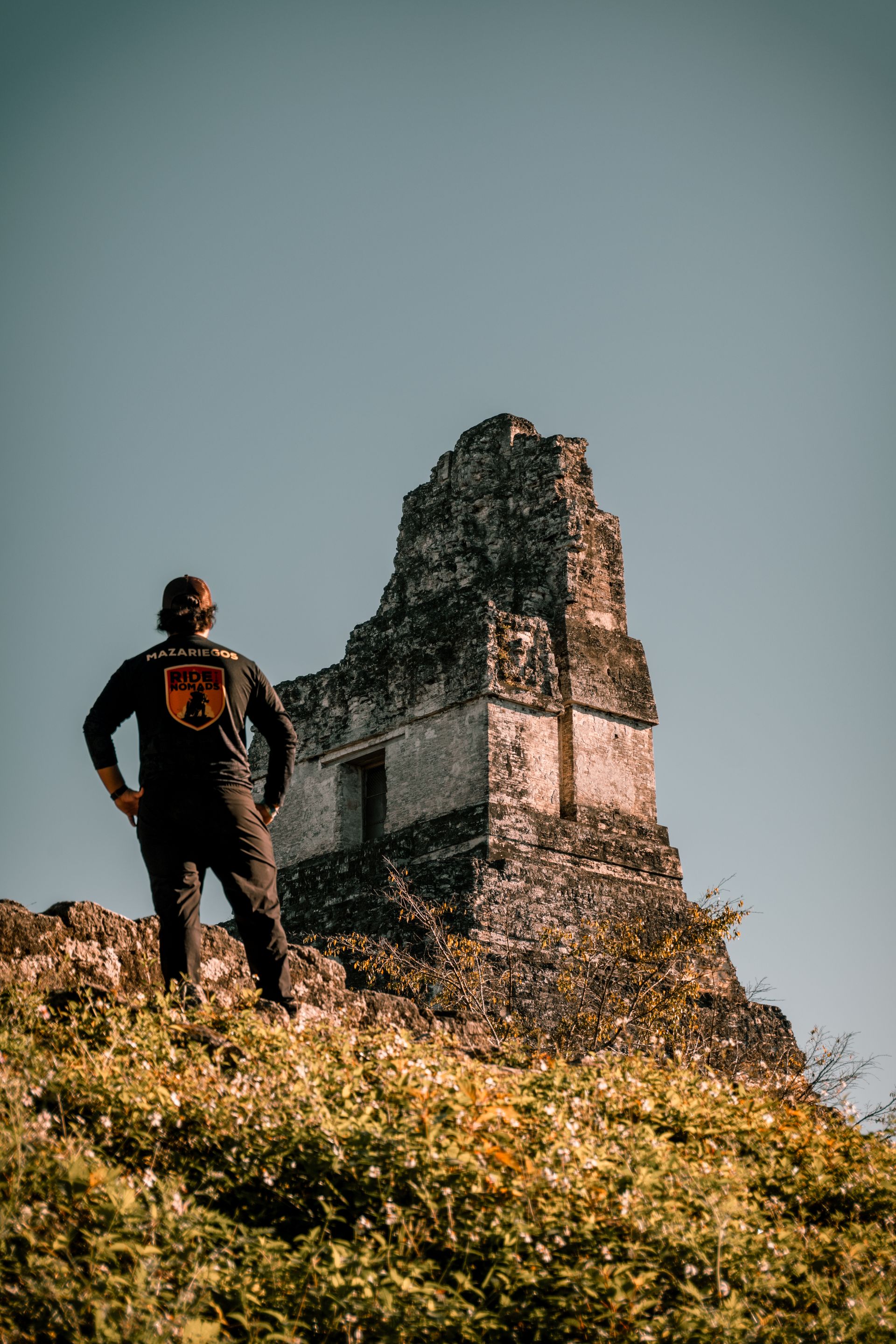 Person standing on a grassy hill beside a weathered stone tower under a clear sky