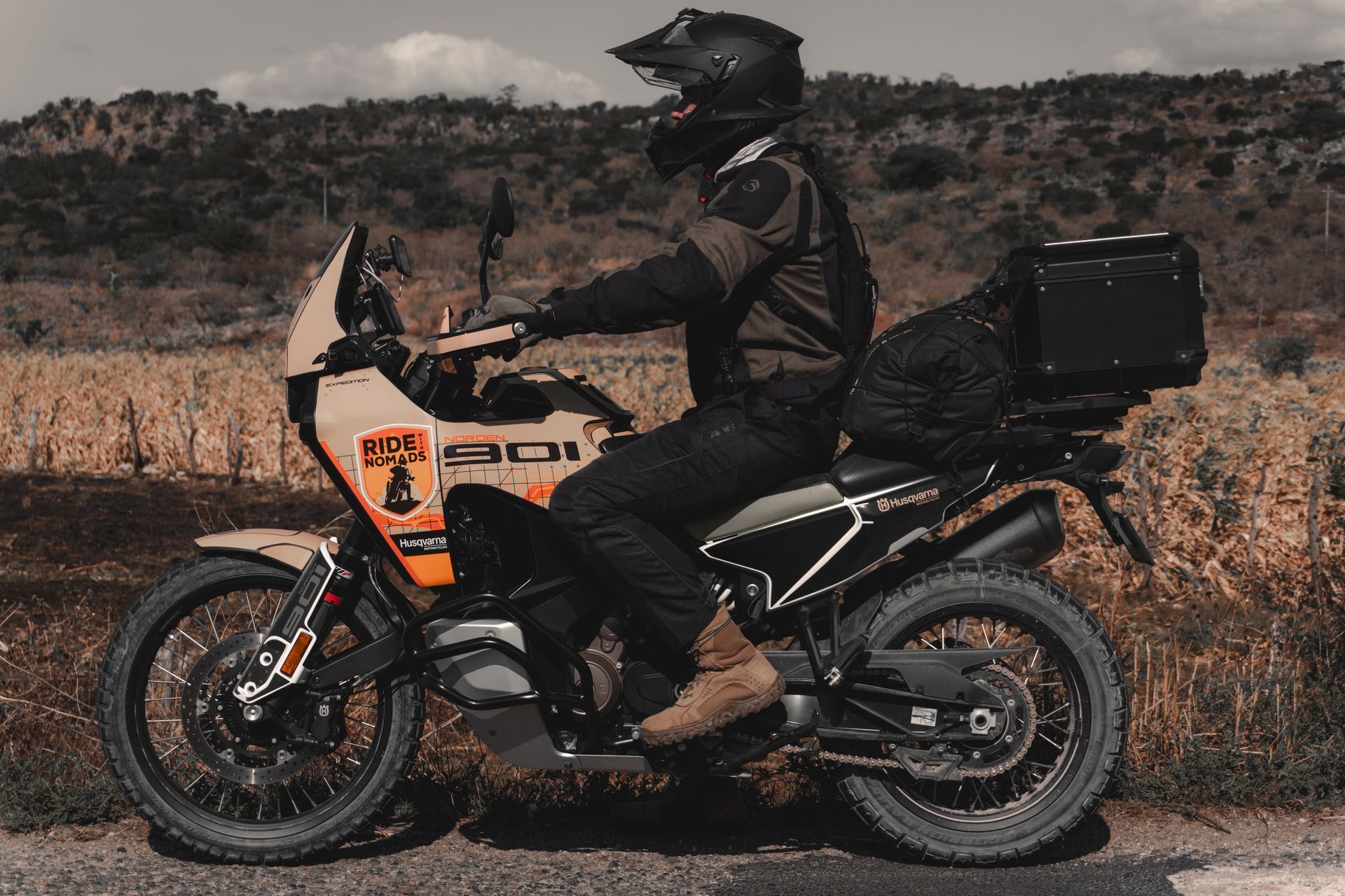 Motorcyclist on an adventure bike in a dry field with hills in the background