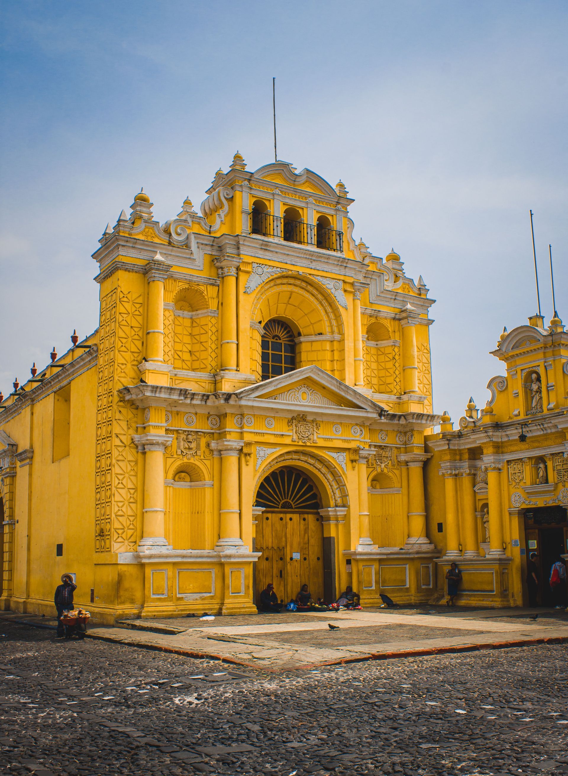 Yellow baroque church facade with ornate towers and a large arched entrance under a blue sky