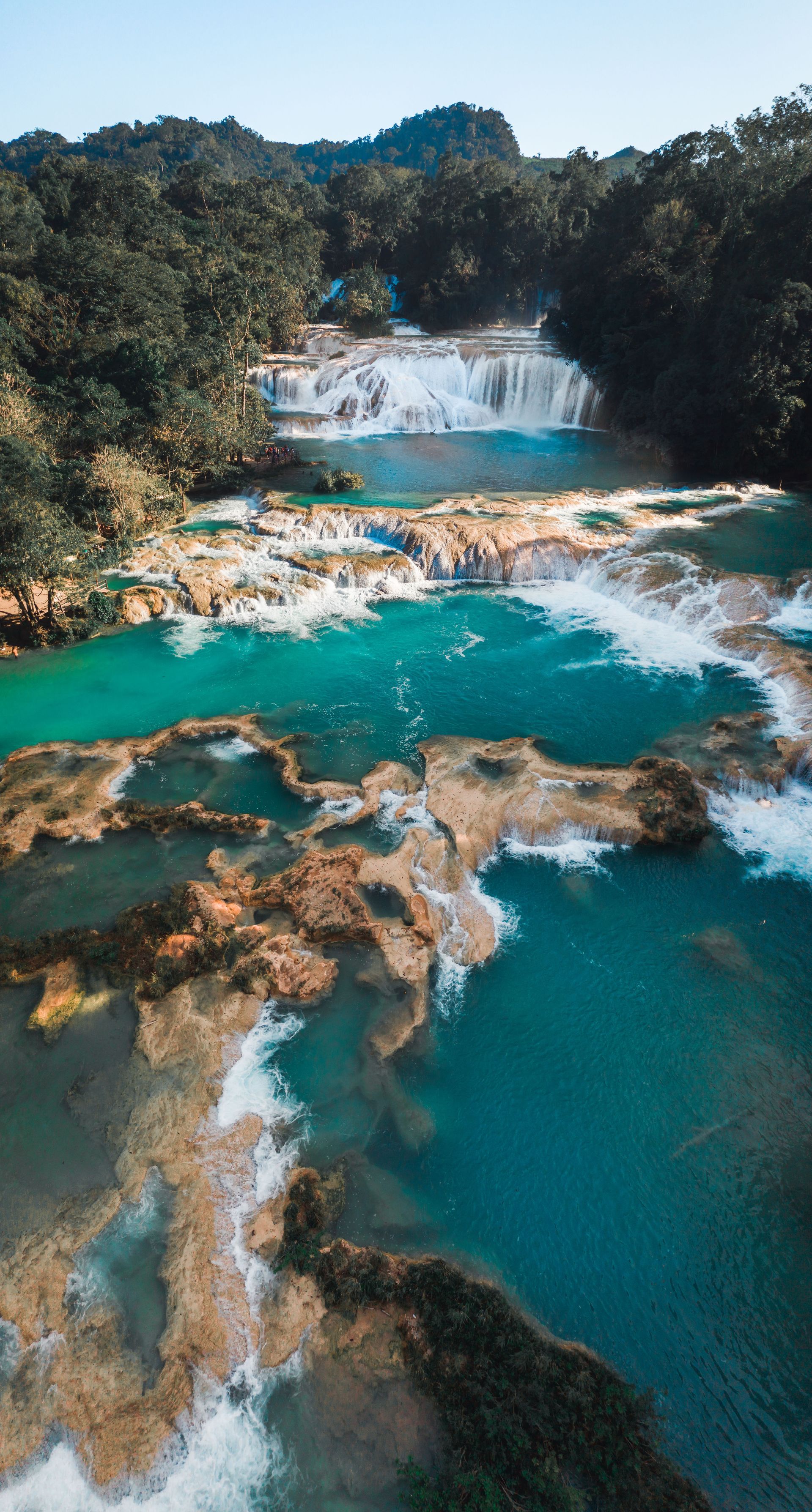 Turquoise waterfall cascading over rocky ledges into a forested river pool