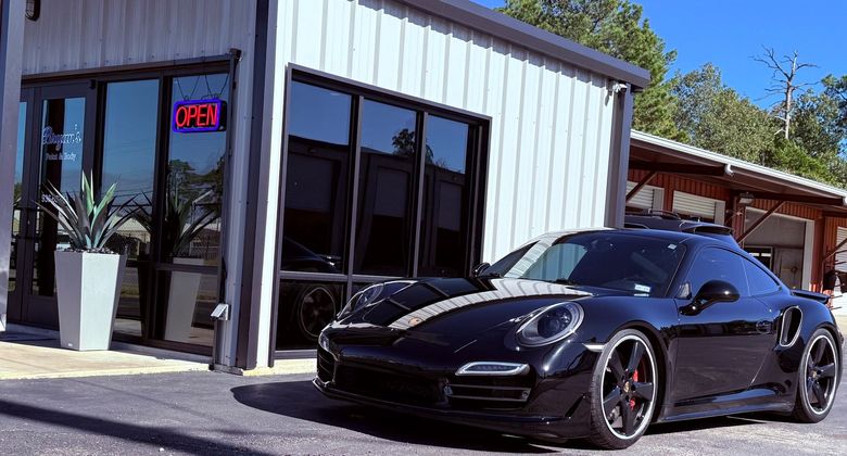Black Porsche sports car parked in front of a modern building with large windows and an