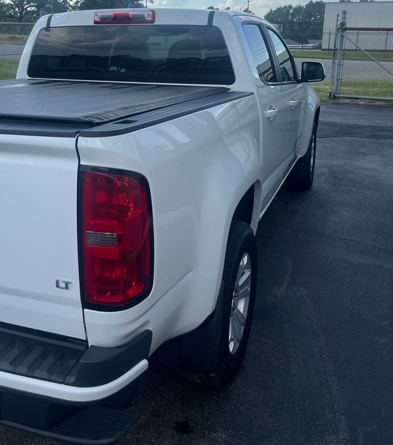 White Chevrolet Colorado pickup truck, rear view, parked on a wet surface.