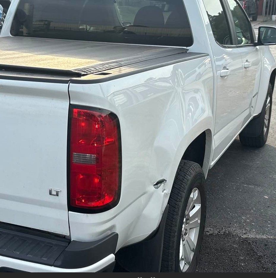 White pickup truck with damage on the rear fender, parked outdoors.