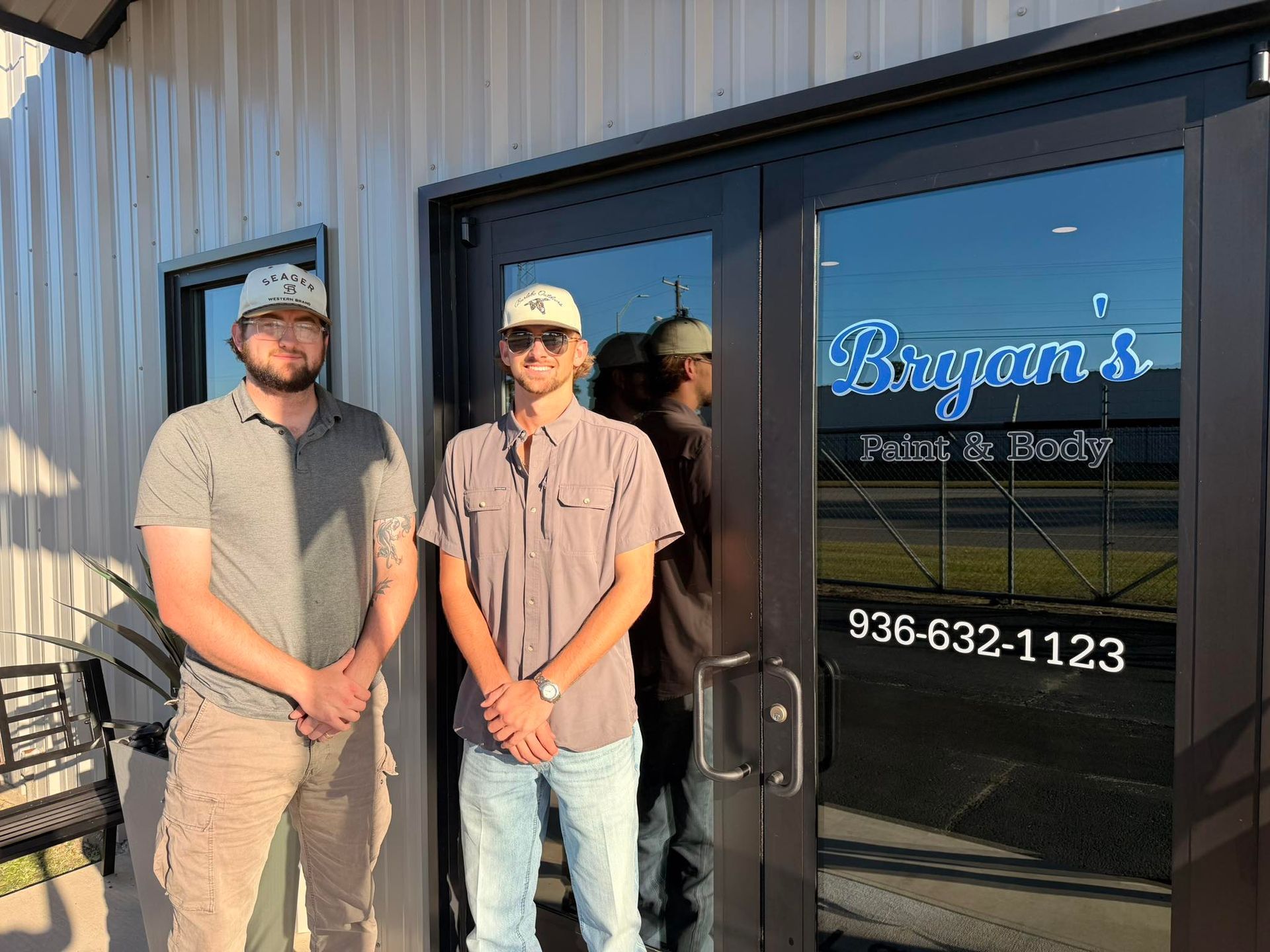 Two men stand in front of a business entrance. The business sign reads 