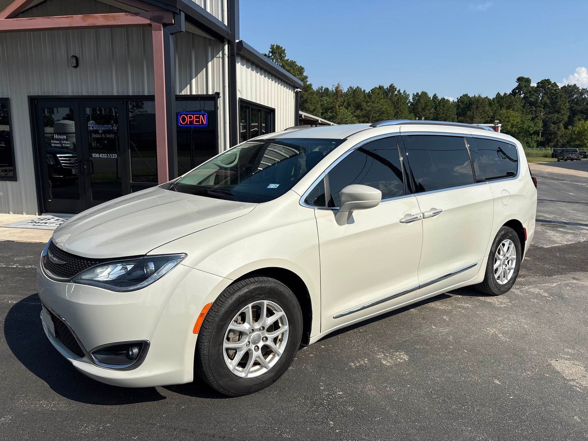 Beige Chrysler Pacifica minivan parked in front of a building on a sunny day.