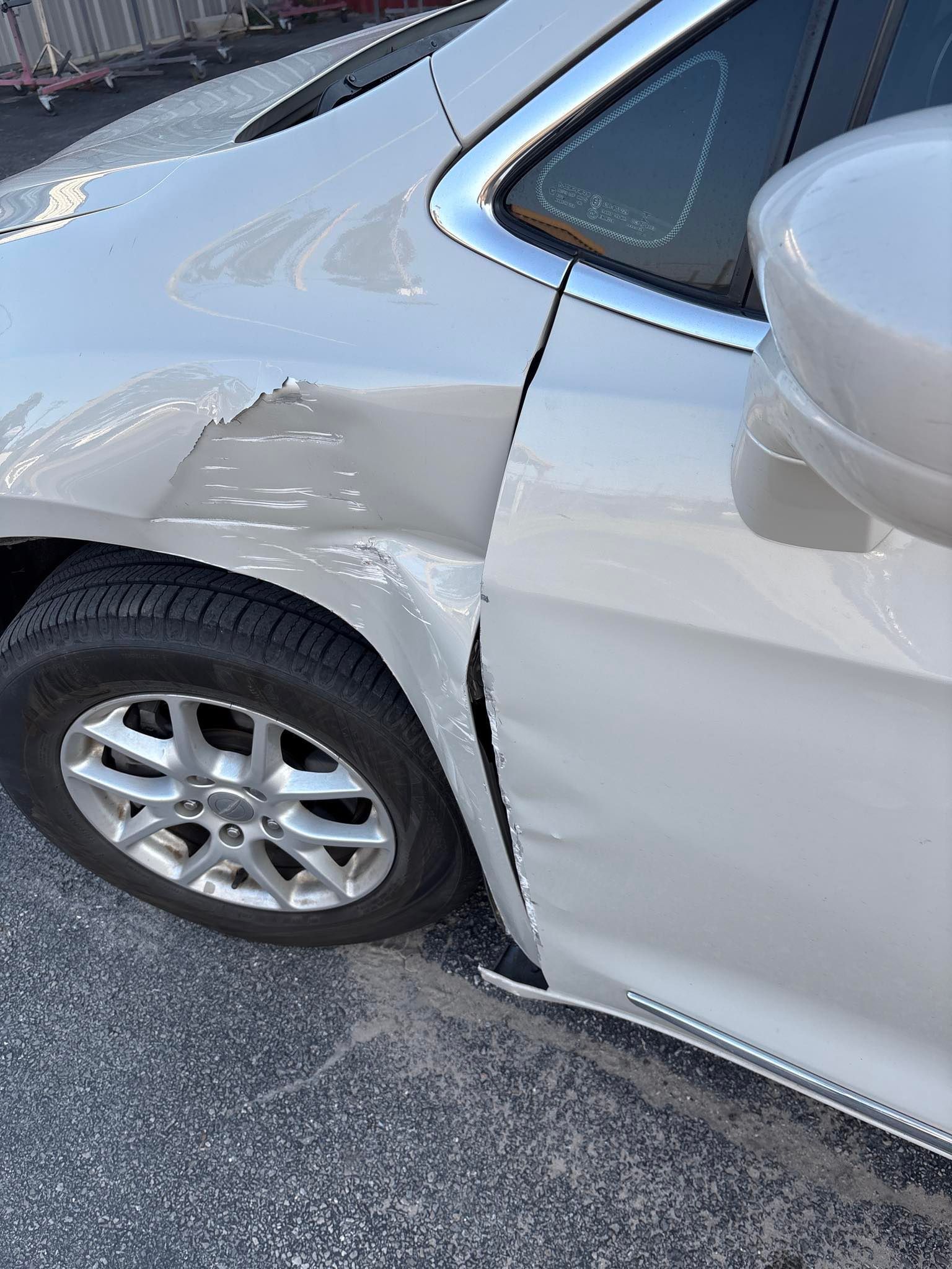 Silver car with significant damage to the front quarter panel and door, near the front tire.