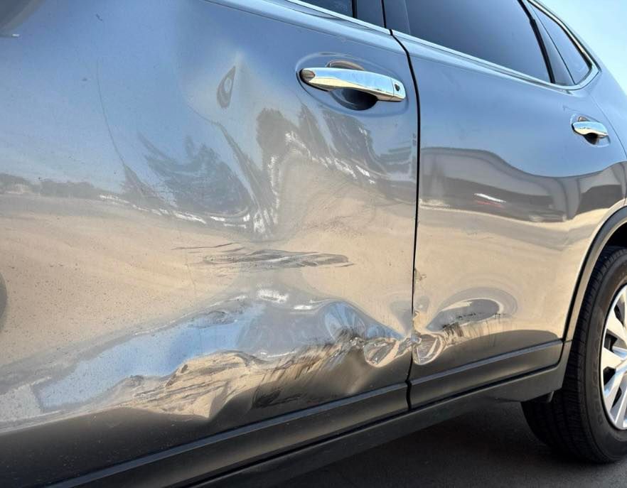Damaged gray SUV door with dents and scratches.