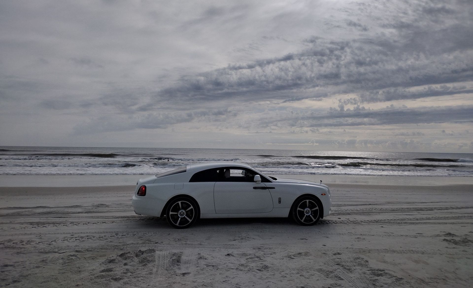 A white car is parked on the beach near the ocean.