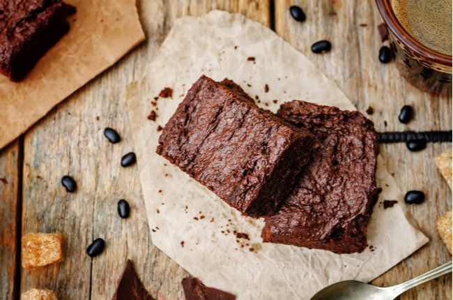 Dois brownies estão sentados em um pedaço de papel sobre uma mesa de madeira.