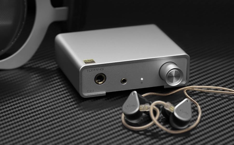 Topping Dx1 Mini Stereo Dac Silver headphone amplifier with wired earphones and large headphones on a textured surface.