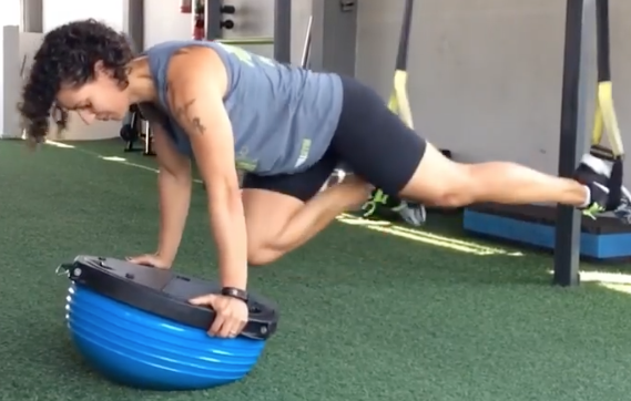 Uma mulher está fazendo flexões em uma bola de equilíbrio azul
