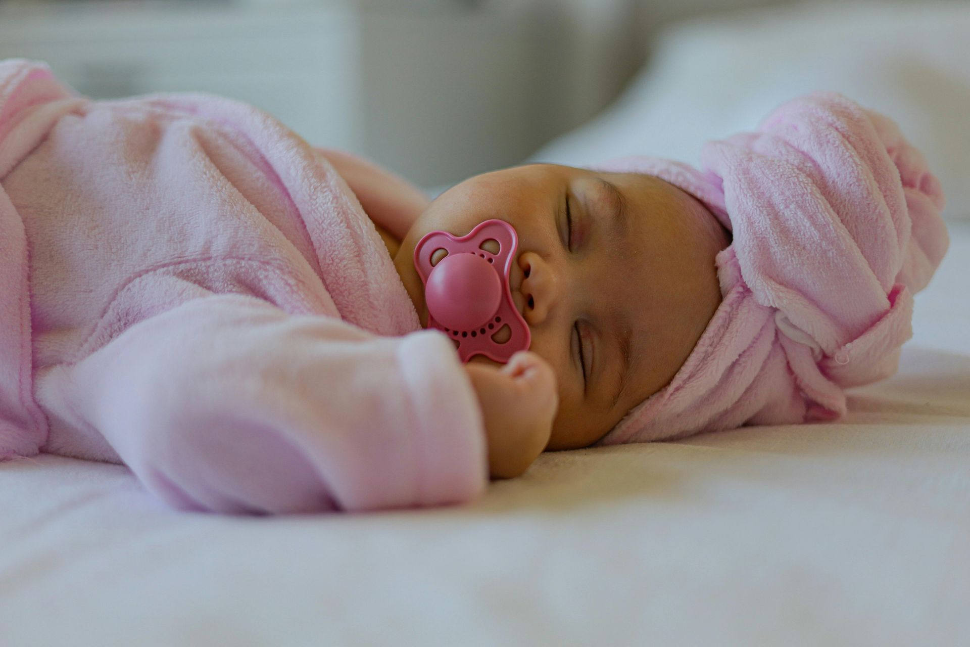Mãe, ser ou não ser? A baby with a pacifier in its mouth is sleeping on a bed.