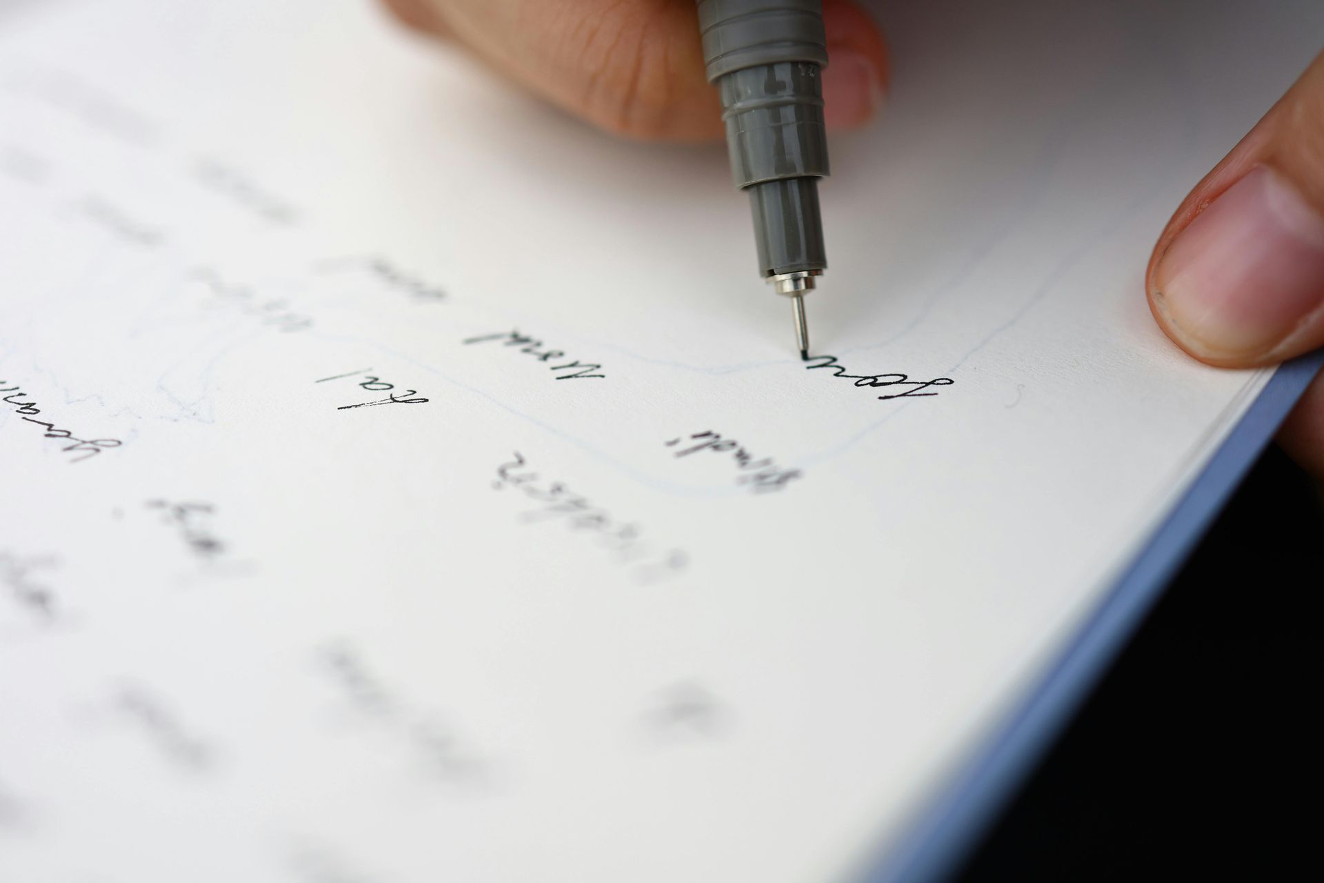 Hand writing with a black pen on a white sheet of paper, close-up shot.