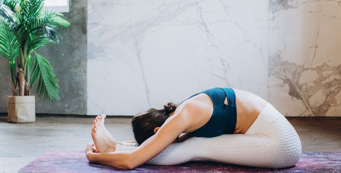 Treino de Yoga em casa A woman is stretching her legs on a yoga mat.