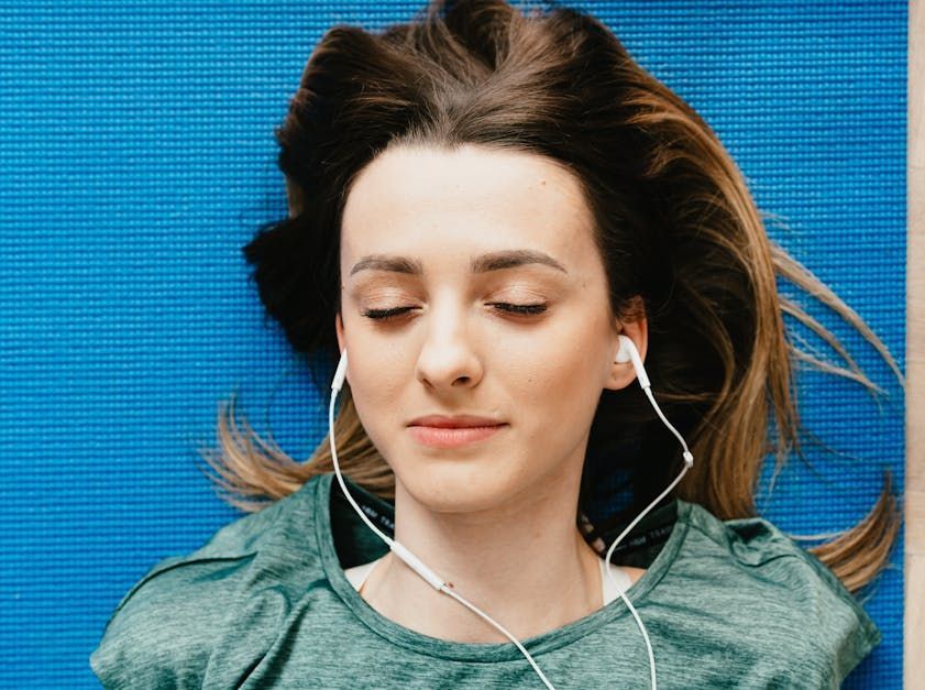 Ser Zen A woman is laying on a yoga mat with her eyes closed and listening to music with headphones.