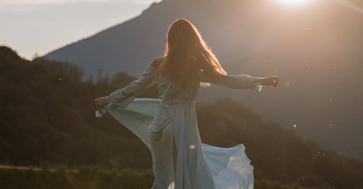 A woman in a white dress is standing in a field with her arms outstretched.
