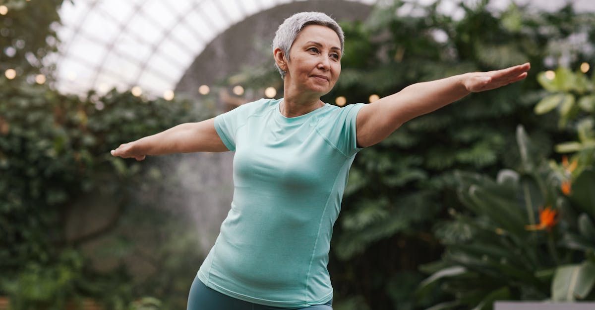 An older woman is practicing yoga in a park with her arms outstretched.