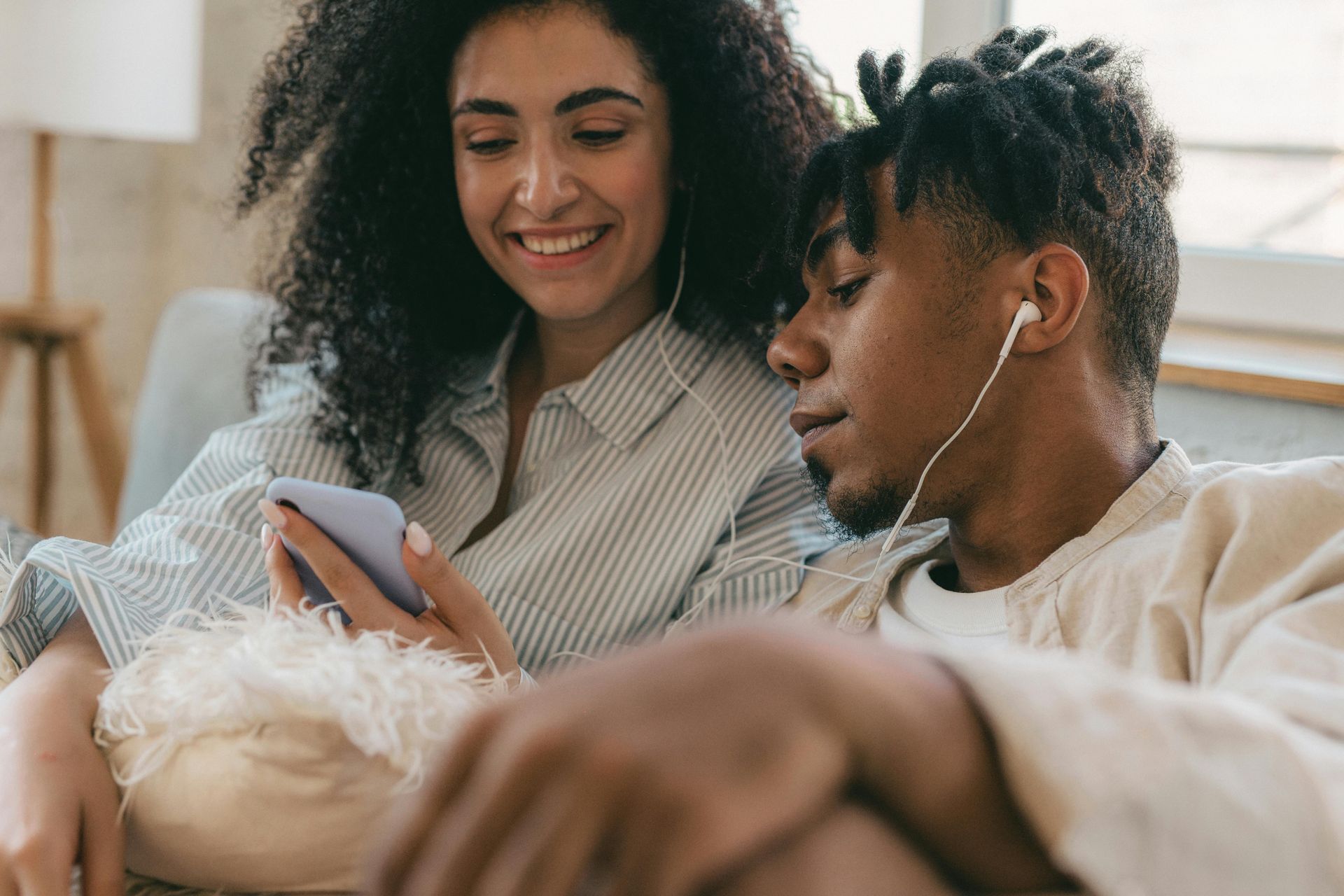 Ouvir música A man and a woman are sitting on a couch looking at a cell phone.