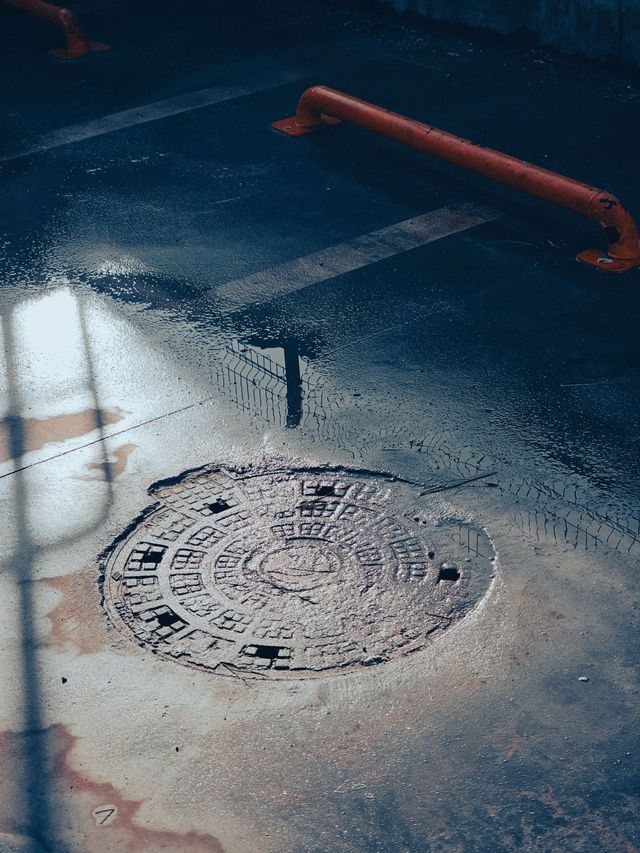 Manhole cover on a wet street with a white lane marking and orange curb barrier nearby