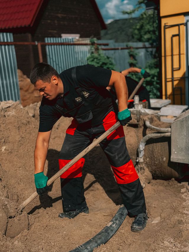 Worker in red and black gloves digging dirt with a shovel at an outdoor construction site