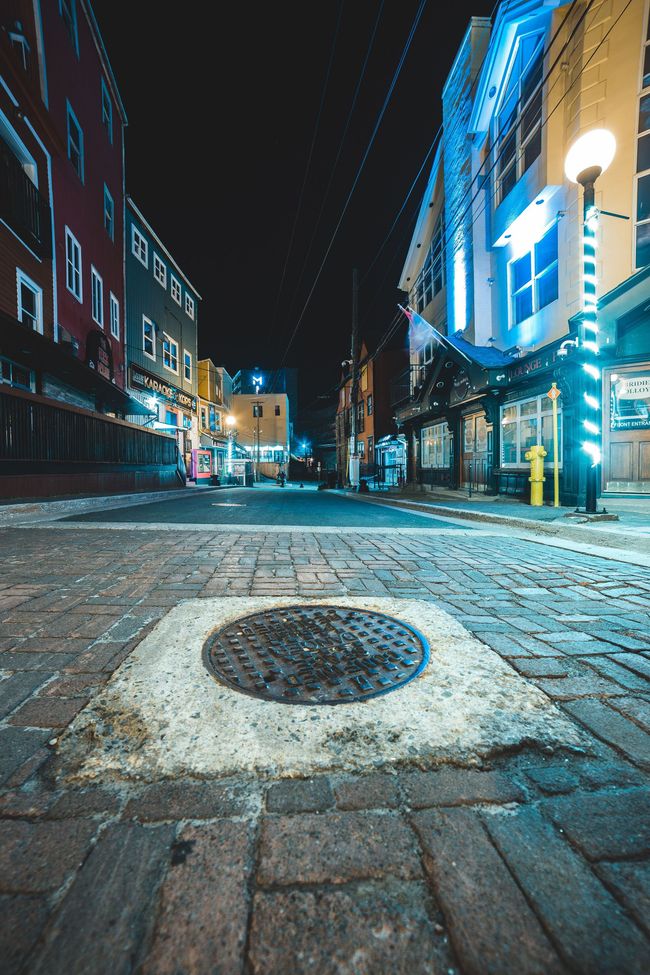 Empty cobblestone street at night, lit by blue neon signs and streetlights.