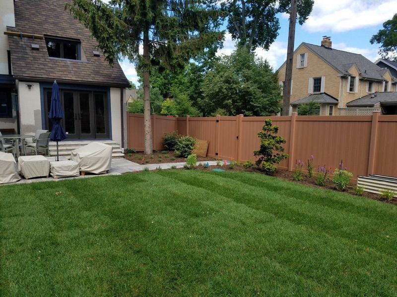 Backyard with brown fence, lush green lawn, patio furniture, and a house.