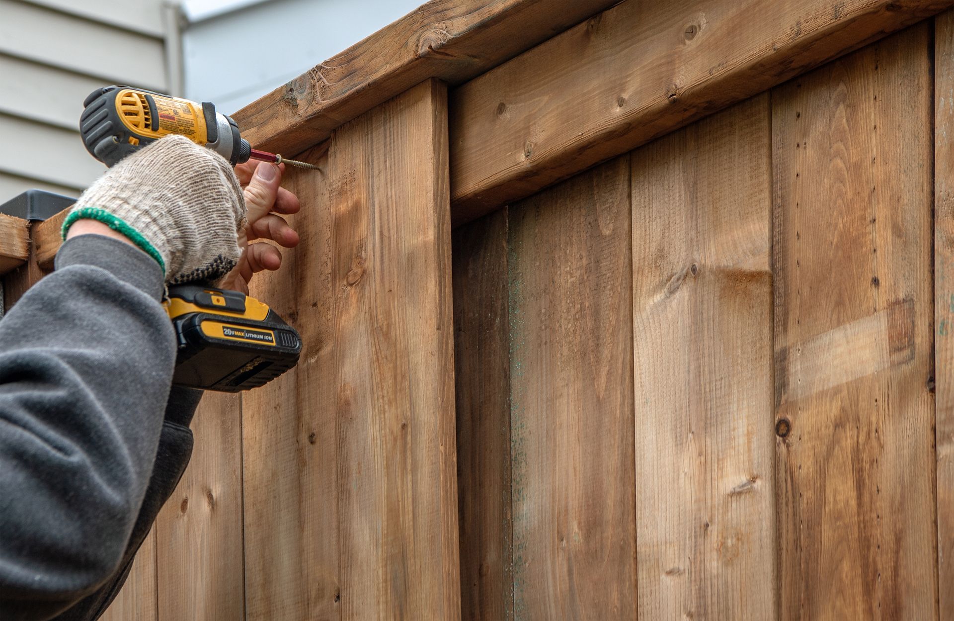 Experienced contractor installing a new wood privacy fence in a backyard.