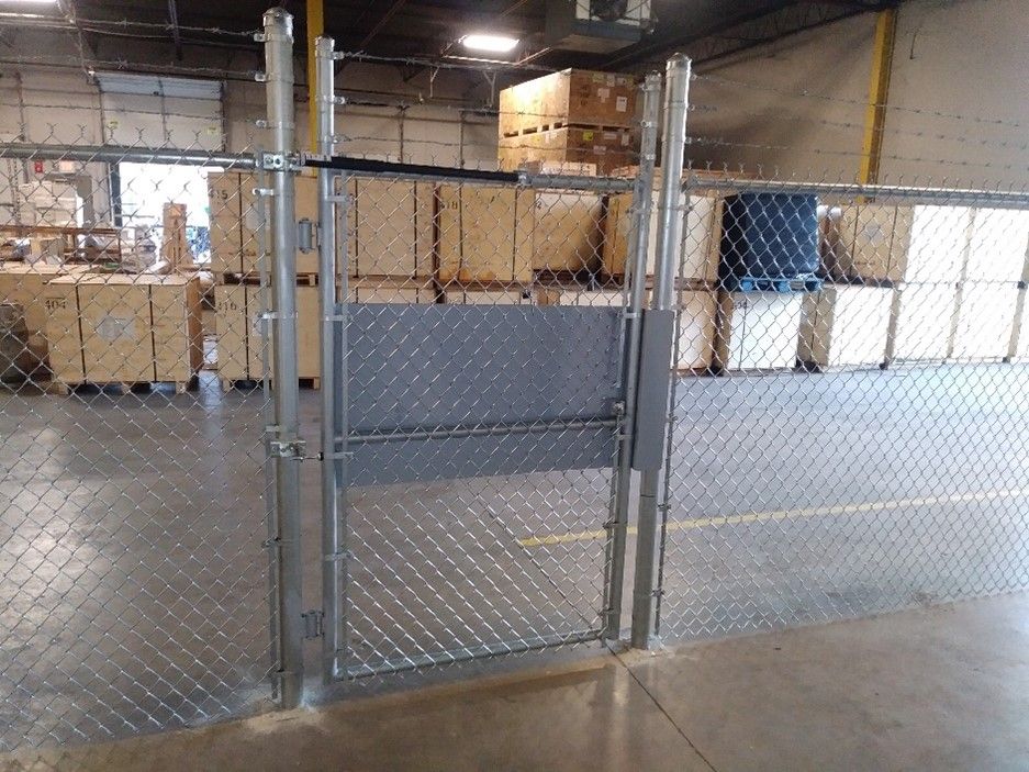 Chain-link fence with a gate, indoors, in a warehouse setting.