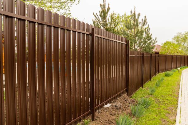 Brown metal privacy fence panels installed along residential property line with green landscaping.
