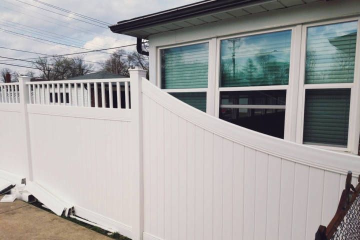 White vinyl fence curves along a building with windows, cloudy sky in background.