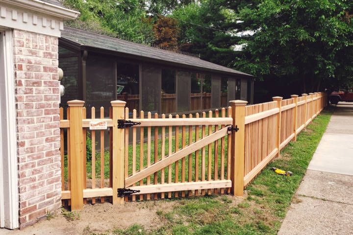 Wooden picket fence with gate next to a brick wall and a house with screening.