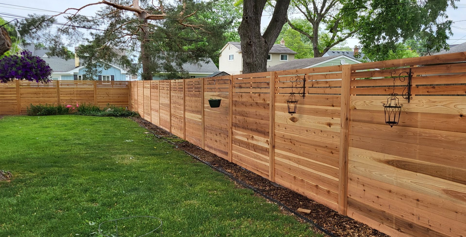 Wooden fence bordering a grassy backyard, with trees and houses visible in the background.