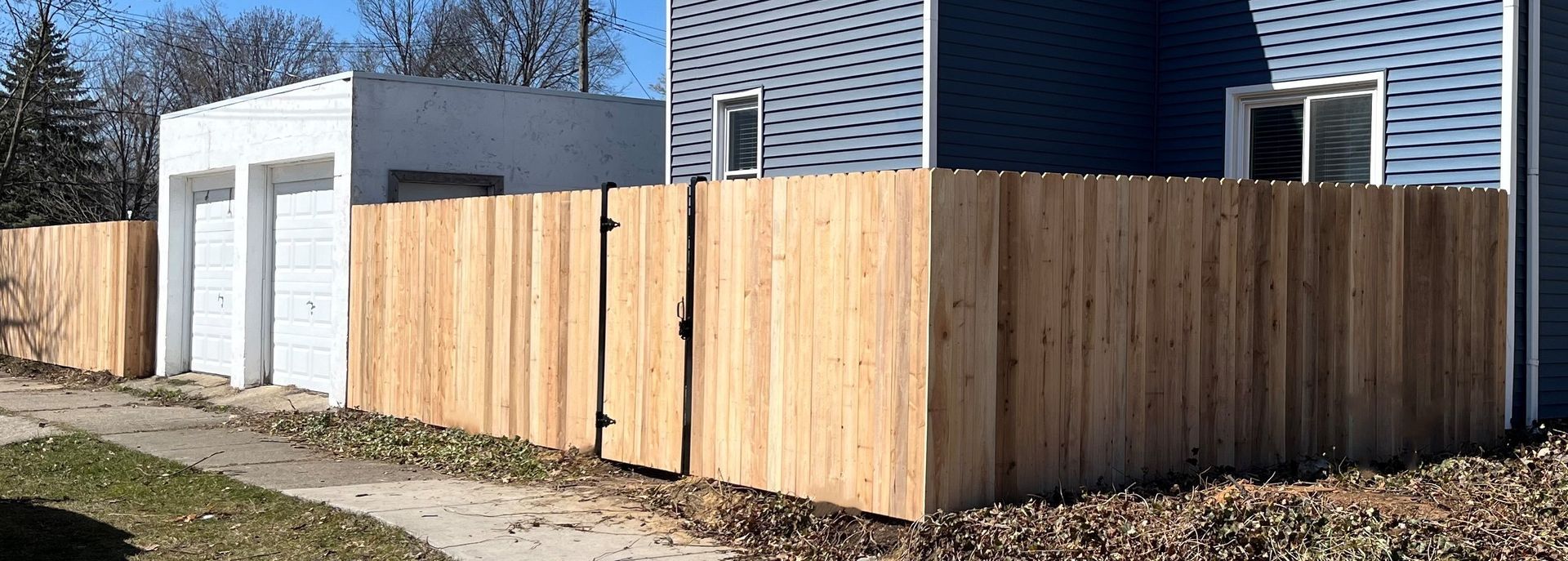 A wooden fence surrounds a house with a white garage on the left.