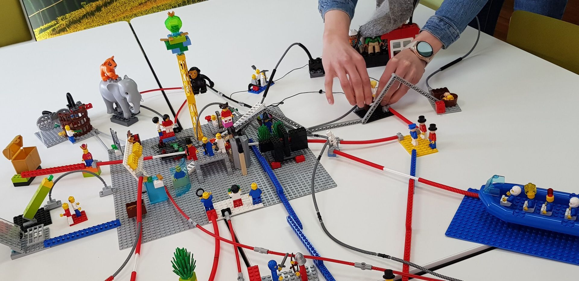 Handen die draden verbinden met een Lego op een witte tafel. 