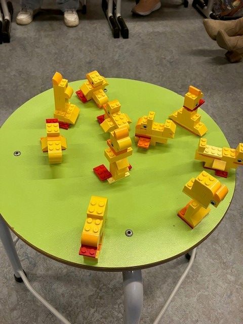 Gele Lego-eendjes op een groene ronde tafel. Sommige staan ​​rechtop, sommige op een rij en andere liggen op hun zij.