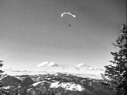 Een paraglider zweeft boven een met sneeuw bedekt berggebied, onder een heldere hemel.
