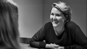 Vrouw lacht en kijkt naar links, waarschijnlijk in gesprek. Zwart-witfoto.