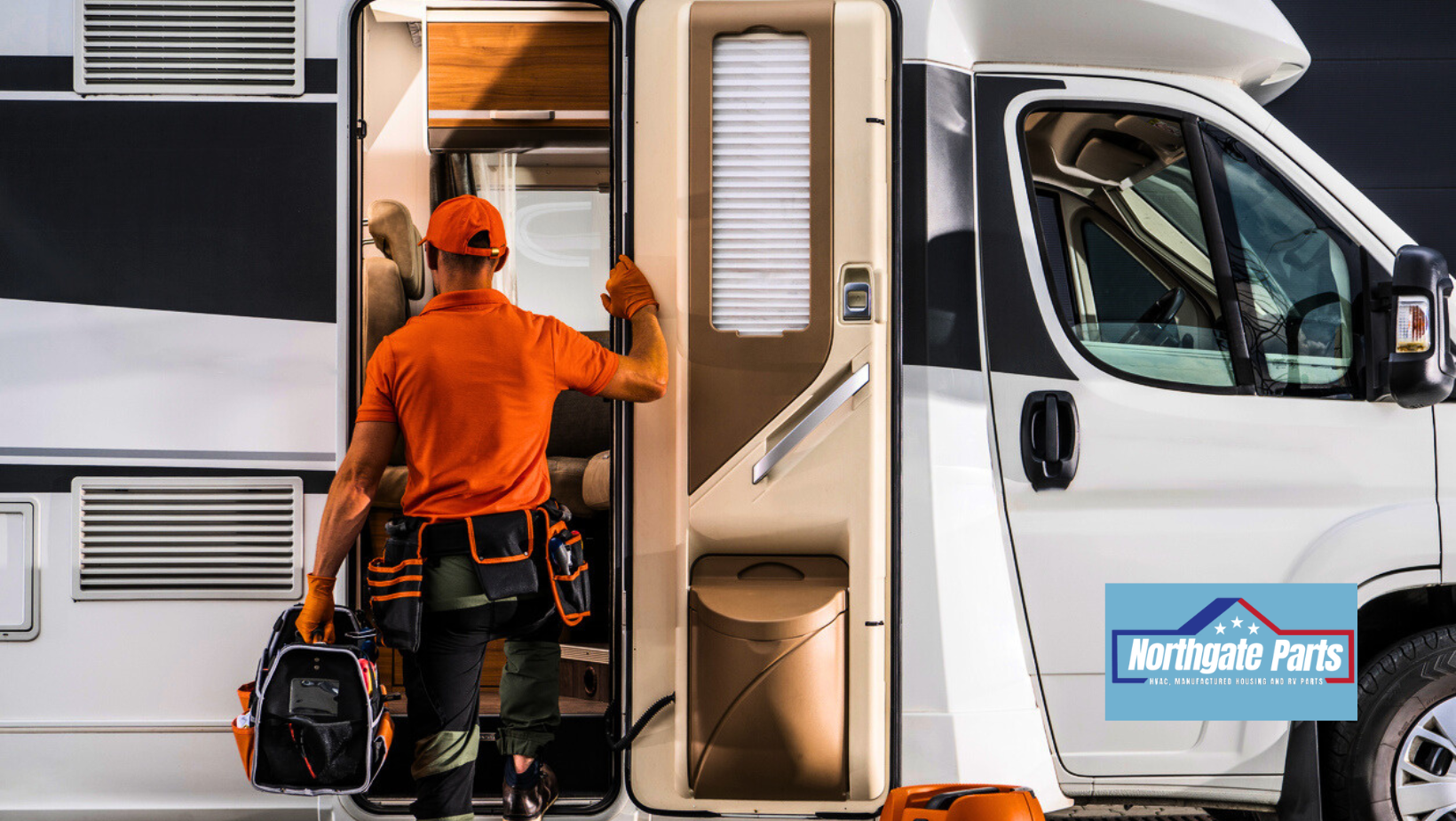 A person in orange work clothes steps into a white RV with a toolbox in hand.