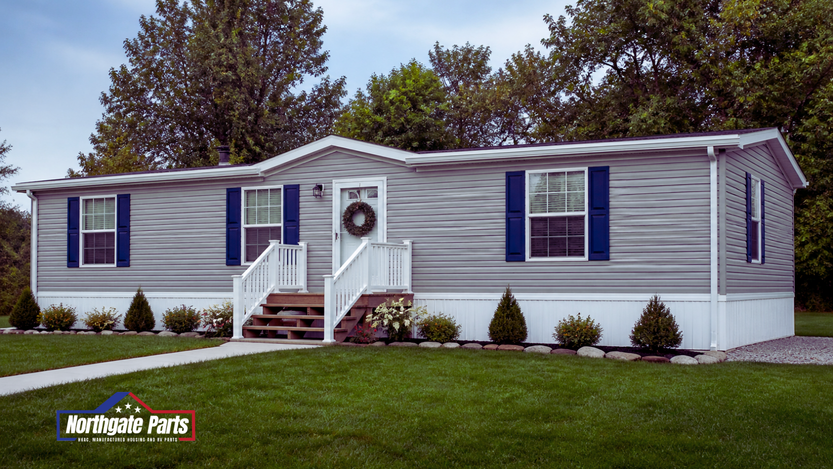 Single-story gray manufactured home with white trim, blue shutters, and a small front porch on a grassy lot.