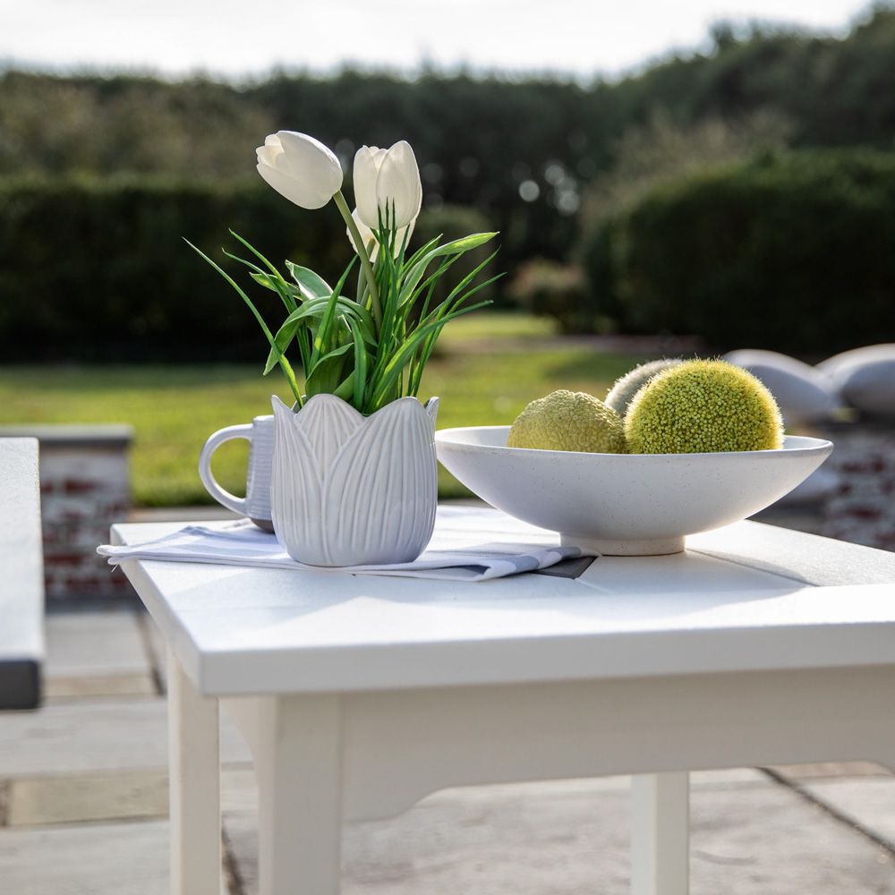 A white table with a vase of flowers and a bowl of fruit on it A white table with a vase of flowers and a bowl of fruit on it