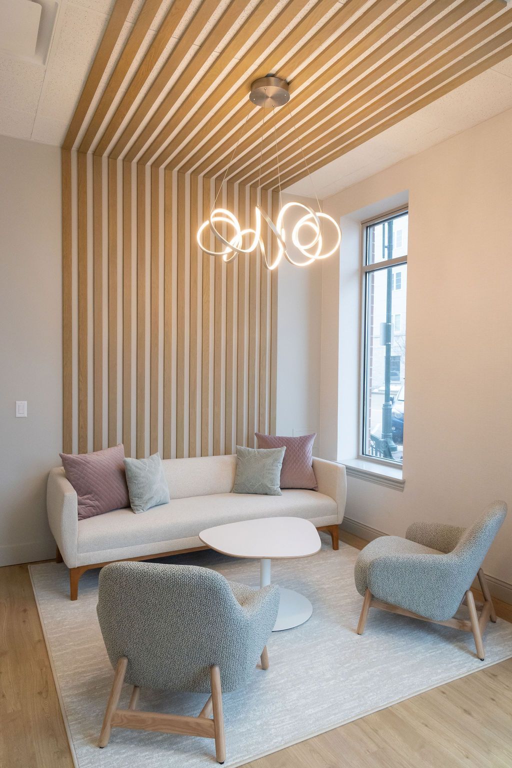 Living room with cream-colored sofa, two armchairs, rug, and decorative ceiling and wall slats.