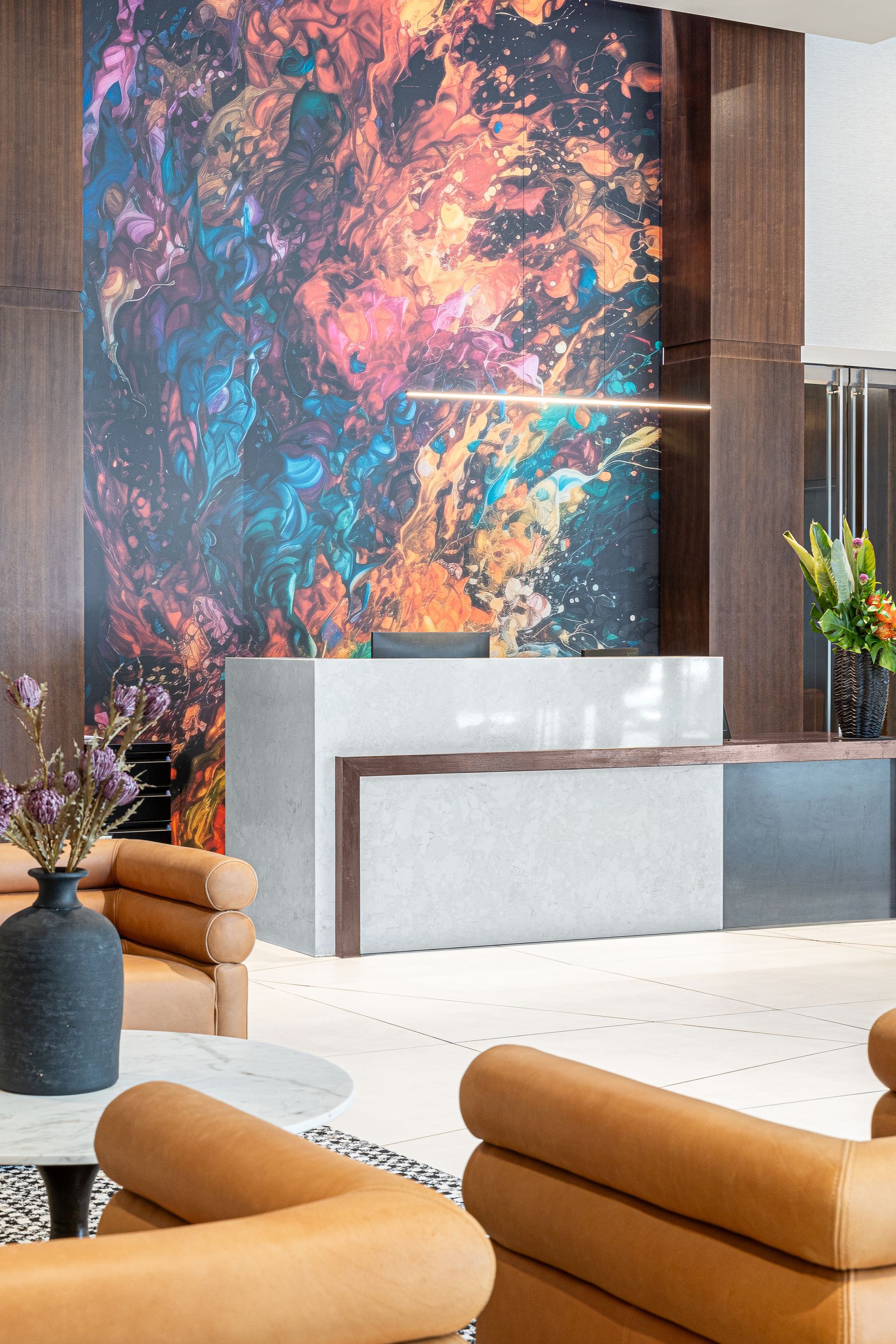 Reception desk with colorful art backdrop, flanked by seating and floral arrangements.