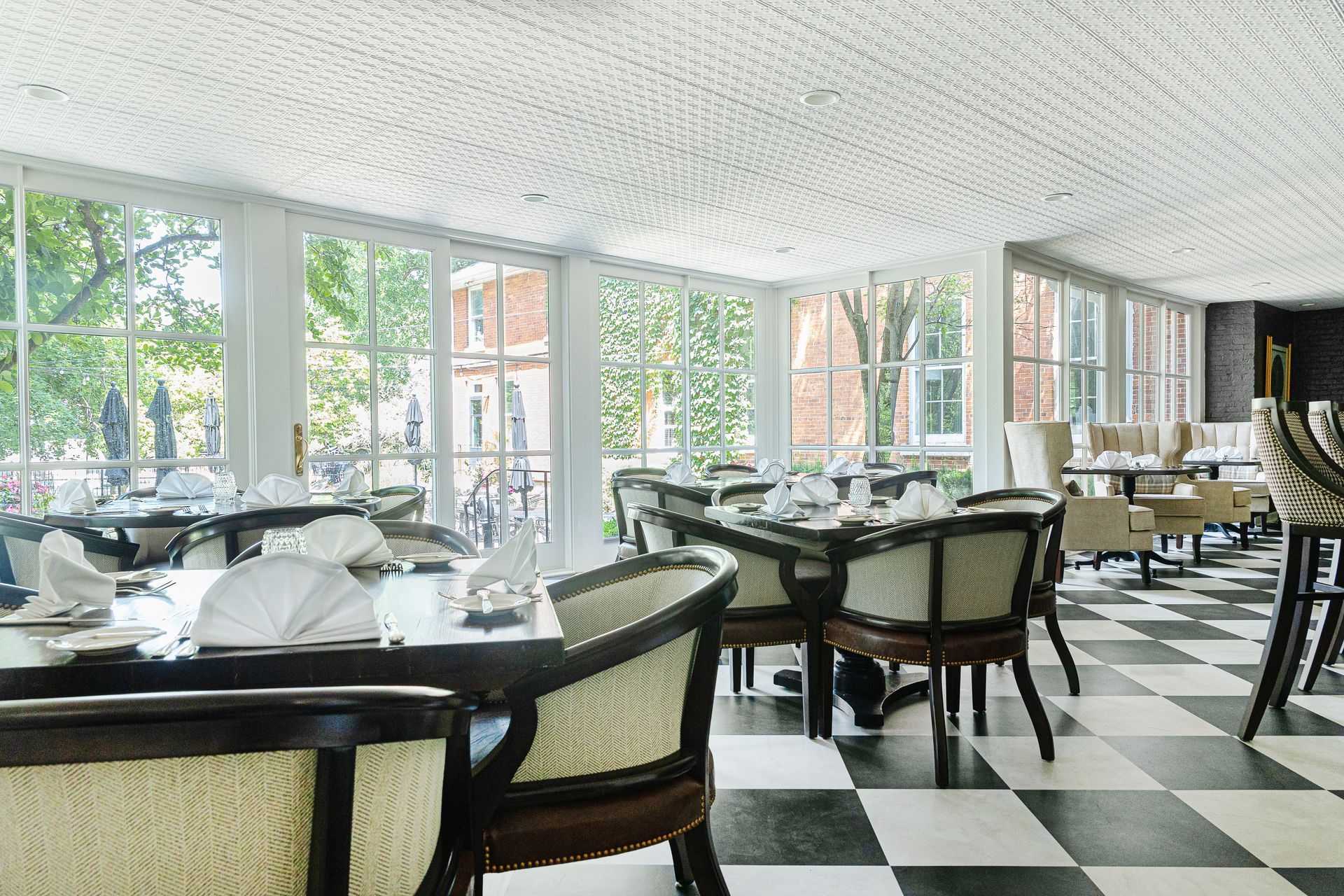 Restaurant dining room with tables set for service, large windows, and checkered floor.