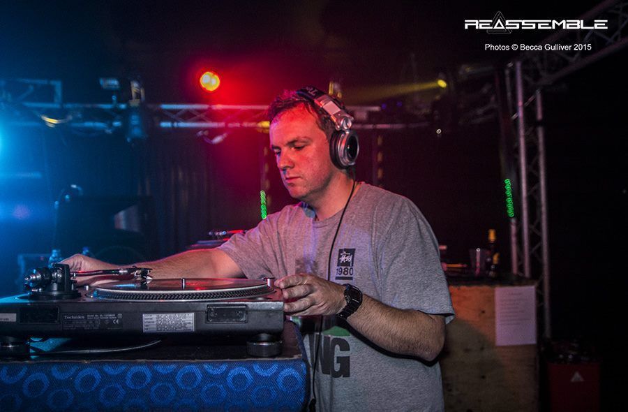 DJ mixing on turntables in a dim nightclub, lit by blue and red stage lights.