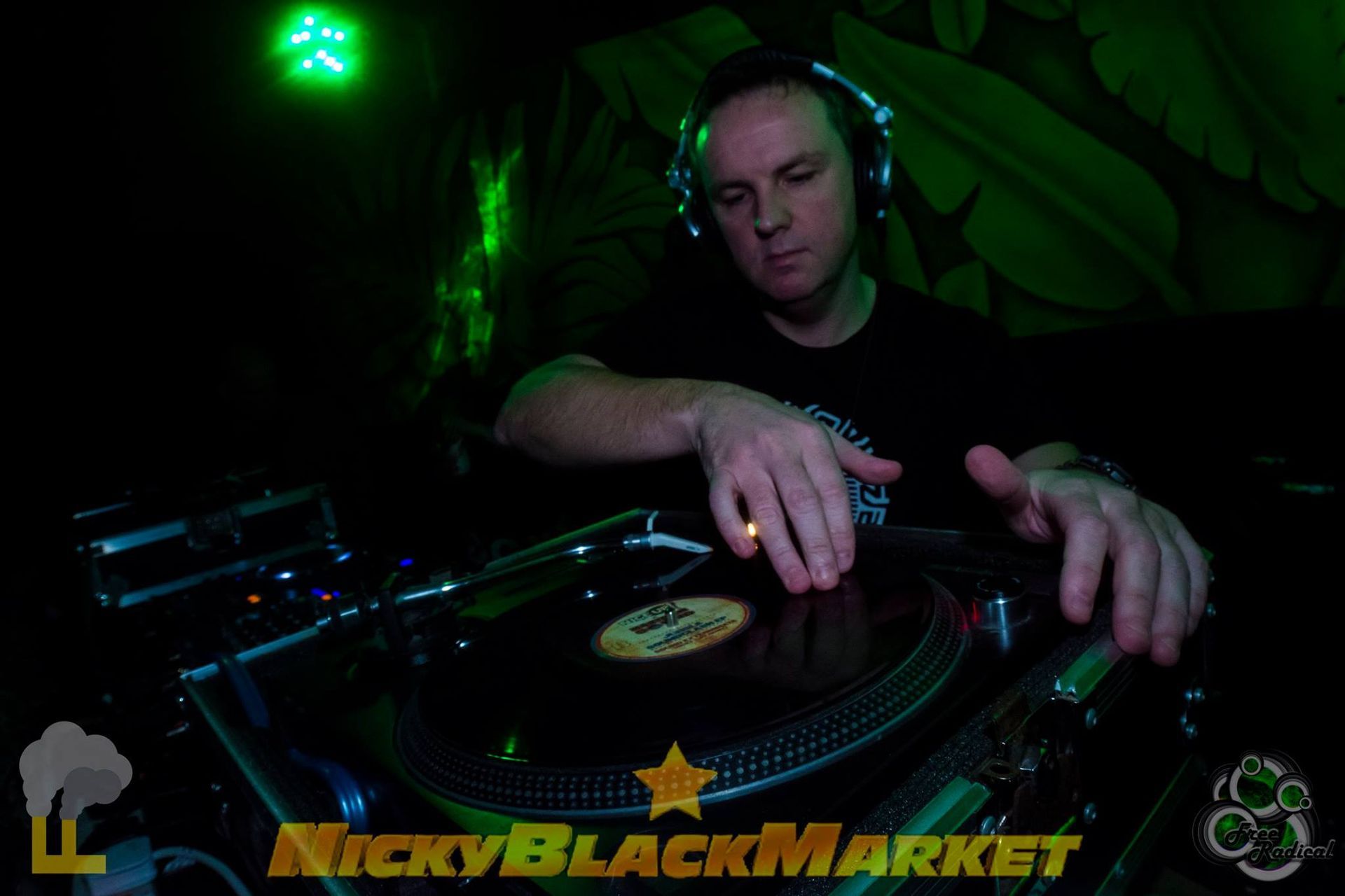 DJ wearing headphones mixing on turntables in a dark club with green lighting and NickyBlackMarket logo