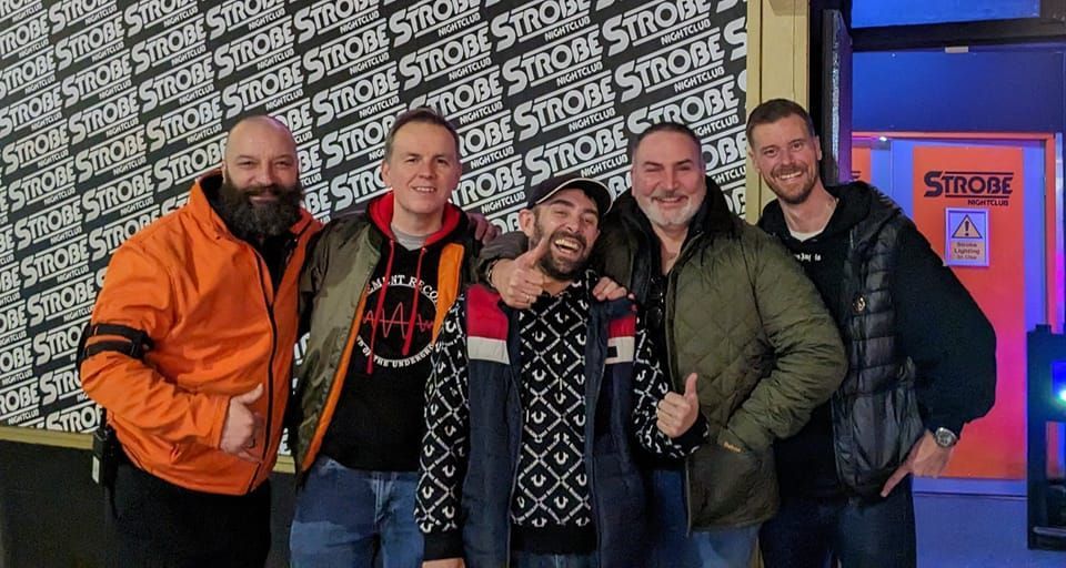 Five people posing together at a SHOT show event backdrop, smiling in casual winter jackets.