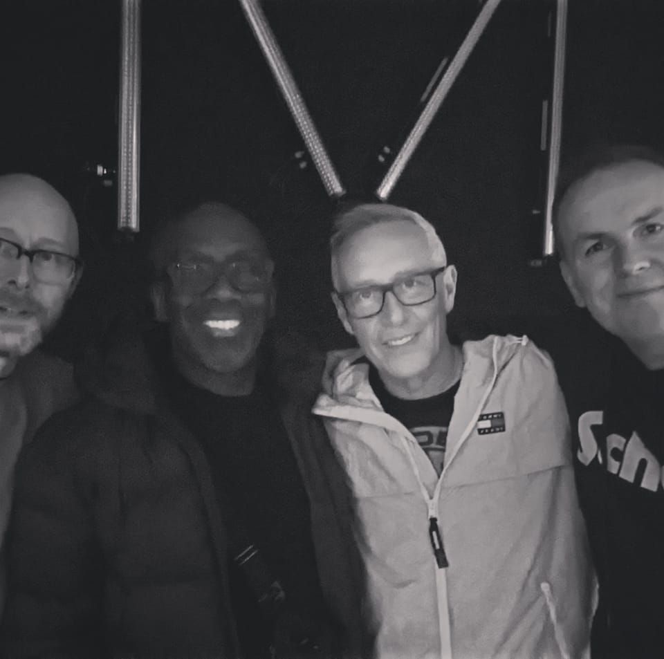 Four people smiling for a black-and-white group selfie indoors.